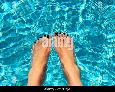 Overhead view of a woman sitting at the edge of a swimming pool dangling her feet in the water Stock Photo