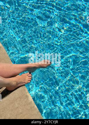 Overhead view of a woman sitting at the edge of a swimming pool dangling her feet in the water Stock Photo