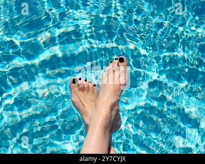 Overhead view of a woman sitting at the edge of a swimming pool dangling her feet in the water Stock Photo