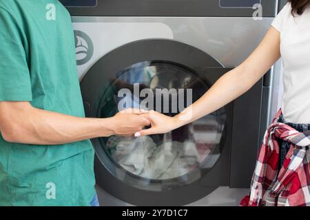 Couple holding hands while doing laundry together at home Stock Photo