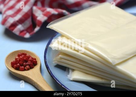 Processed cheese, slices of processed cheese wrapped in plastic and spoon with pink berries, red pepper Stock Photo