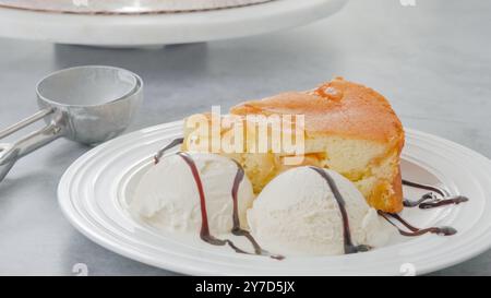 Slice of a freshly baked apple cake with whipped cream topping, served with vanilla ice cream and chocolate close-up on a white plate Stock Photo