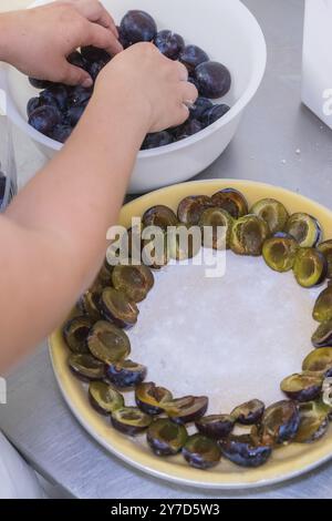 Person places plum halves on a round pastry base, preparing a cake Stock Photo