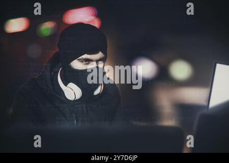 Angry computer hacker weared balaclava stealing data from laptop in front of black background and blue light. close portrait. hack concept Stock Photo