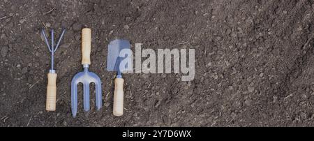 Hand garden tools on black fertile soil. Preparation for planting seedlings. Banner panorama Stock Photo