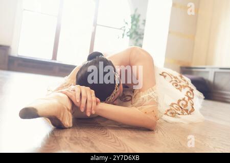 A ballerina in a white tutu warming up before training lying on the studio floor Stock Photo