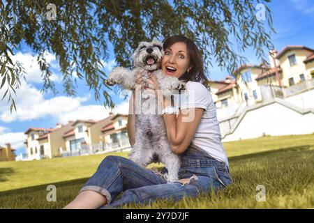 Caucasian joyful woman playing with her beloved dog in the park. The concept of love for animals. best friends. Dog breed Schnauzer Stock Photo