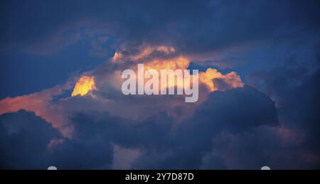 Orange clouds in the center of the dark blue, illuminated by the sun at sunset. Abstract sky at sunset Stock Photo