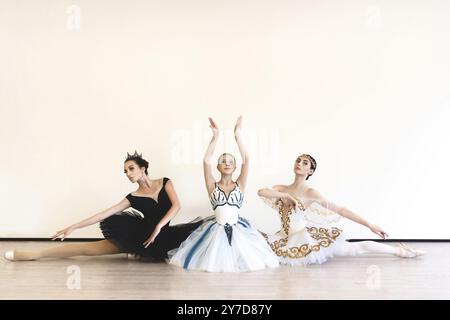 Three young ballerinas perform paired exercises against a white background in the studio Stock Photo