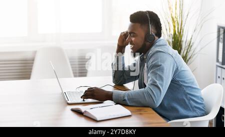 Cheerful manager wearing headset and using laptop, speaking with client Stock Photo