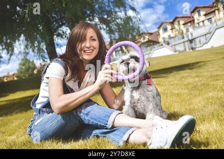 Caucasian joyful woman playing with her beloved dog in the park. The concept of love for animals. best friends. Dog breed Schnauzer Stock Photo