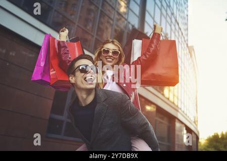Happy couple shopping together and having fun. Boyfriend carrying his girlfriend on the piggyback Stock Photo