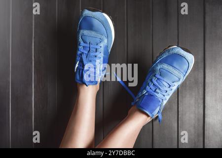 Close up fashion image of woman's feet, wearing sport sneakers on wooden background. lazy woman concept, rest concept Stock Photo