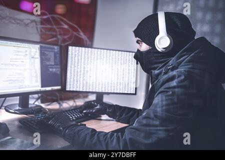 Young Teenage Hacker man Using her Computer to Organize Malware Attack on Global Scale. She's in Underground Secret Location Surrounded by Displays an Stock Photo