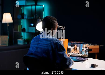 Young black woman engrossed in video call with multiracial people, having online meeting. African american person with digital laptop is seated at desk on conference call with fellow classmates. Stock Photo