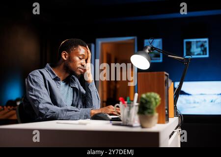 Developer feeling exhausted trying to meet deadline, working hard to finish report in time. African american person being under stress with pressure from executive board, solving important problems. Stock Photo
