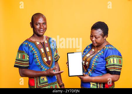 Black man and woman advertisers holding digital tablet with white screen, presenting new portable gadget. Smiling couple showcasing device with blank touchscreen mockup and looking at camera Stock Photo