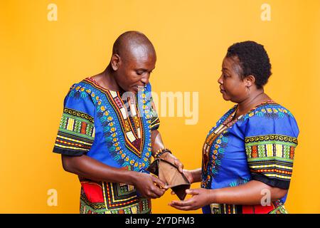 African american man looking in open wallet with no money inside while having conflict with wife. Annoyed woman showing empty purse to husband while discussing financial trouble Stock Photo