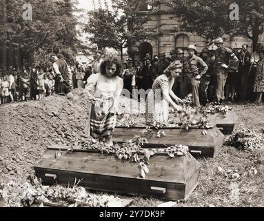 German girls place flowers on the coffins of seven Russian victims hung by their captors in Muehlheim.  Actions like this were part of the Denazification process. This process was an attempt to rid Germany and Austria culture and society of nazi influence and ideology. A part of the process included confronting the public with the evidence of the crimes that were carried out in their area. Stock Photo