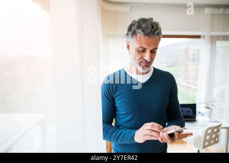 Homeoffice for handsome man. Man working in his office in home, scrolling on smartphone. Telecommuting. Stock Photo