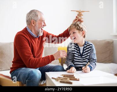 Grandfather spending time with grandson, taking care of him while parents are at work. Boy and grandpa playing with wooden plane toy. Stock Photo