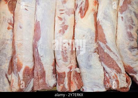 Row of pork ribs are displayed in a butcher shop. The ribs are white and have a pinkish hue Stock Photo
