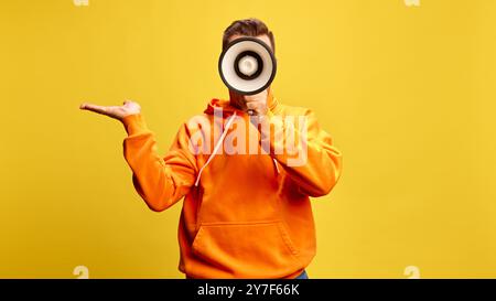 Man shouting to megaphone, shrugging as if making statement or raising awareness against sunny yellow background. Stock Photo