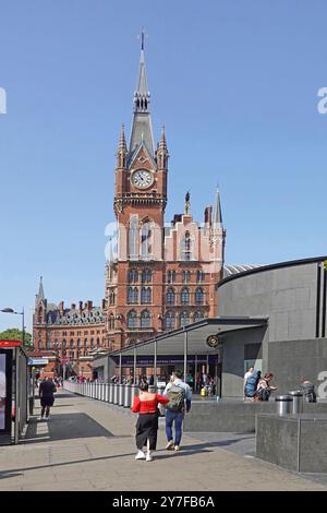 Couple strolling pavement entrance to Kings Cross underground train station walking towards St Pancras Station Victorian clock tower London England UK Stock Photo