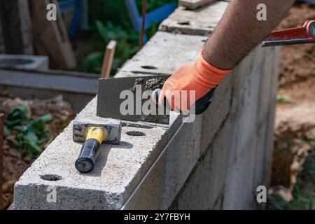 A bricklayer works on blocks to build a wall on a construction site with concrete, a trowel, a level and a grinder Stock Photo