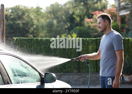 Man cleaning car with water using hosepipe in the garden Stock Photo