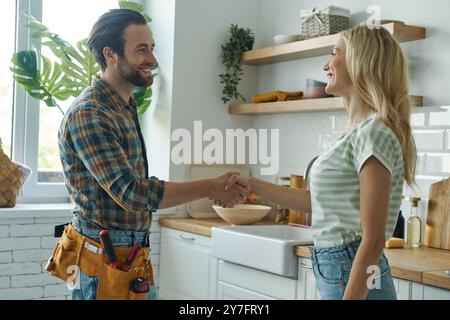 Beautiful young woman shaking hand to male plumber while standing at the kitchen Stock Photo