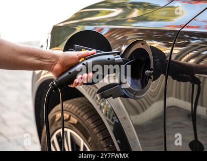 Close up of hand plugging EV charger into electric vehicle outside. Stock Photo