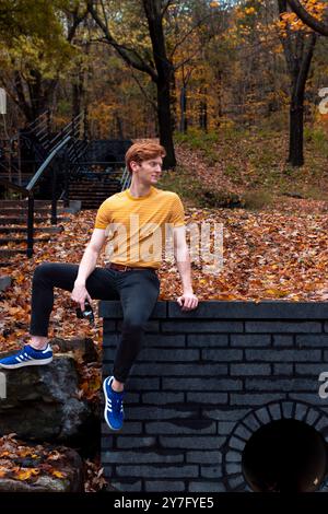 A young man in a yellow shirt relaxes on a stone wall Stock Photo