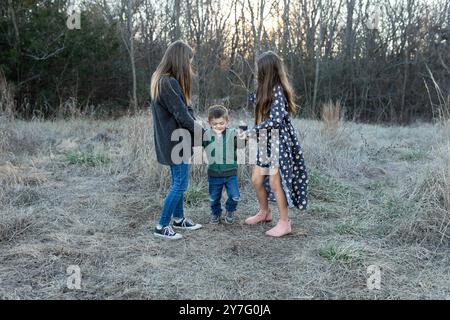 Two girls play with  young boy outside in a grassy field during sunset Stock Photo