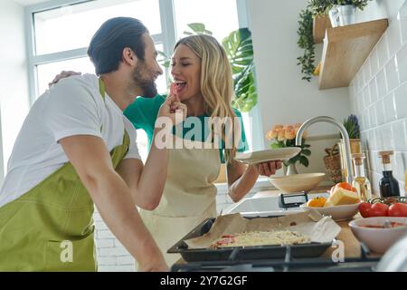 Cheerful young couple making homemade pizza at the kitchen together Stock Photo
