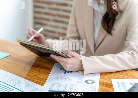 Happy young business woman working on her project at the office, checking data on her tablet and printed notes Stock Photo