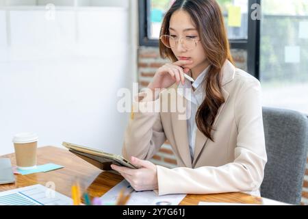 Happy young business woman working on her project at the office, checking data on her tablet and printed notes Stock Photo
