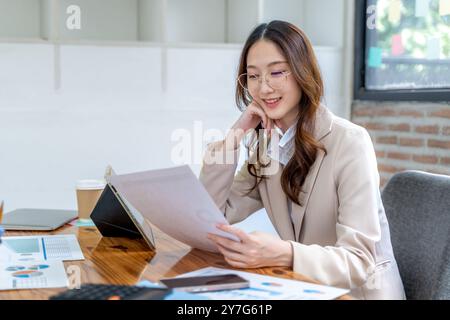 Happy young business woman working on her project at the office, checking data on her tablet and printed notes Stock Photo