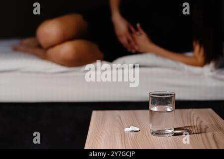 Sad young woman wearing nighty shirt suffering from menstrual pain, feeling sick to her stomach, holding belly. Girl having abdominal cramps during pe Stock Photo