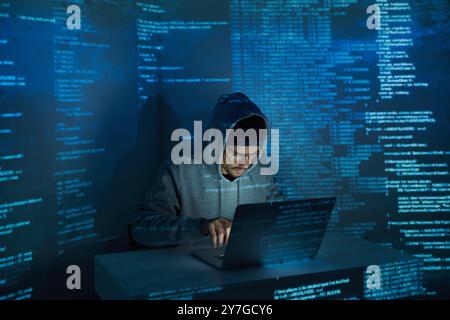 Confident young man in hooded shirt using computer against dark background Stock Photo