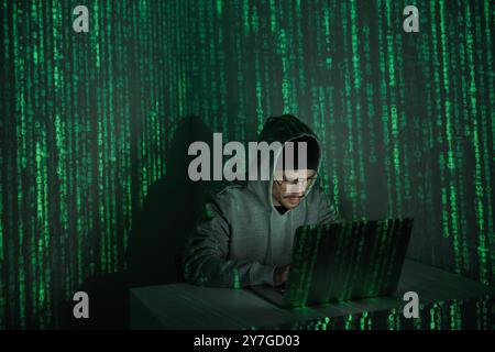 Confident young man in hooded shirt using computer against dark background Stock Photo