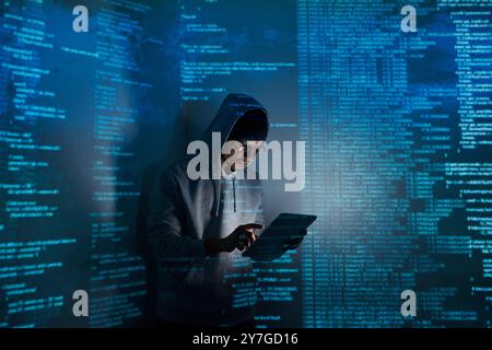 Confident young man in hooded shirt using digital tablet while standing against dark background Stock Photo