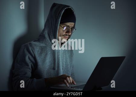 Confident young man in hooded shirt using computer while working late Stock Photo