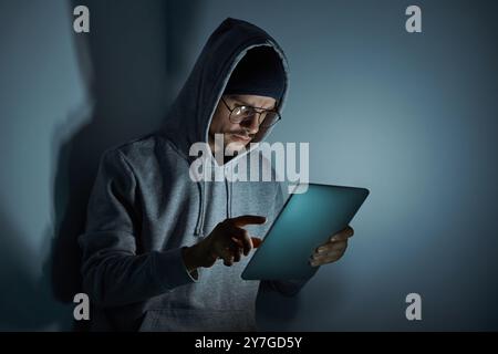 Confident young man in hooded shirt using digital tablet while working late Stock Photo