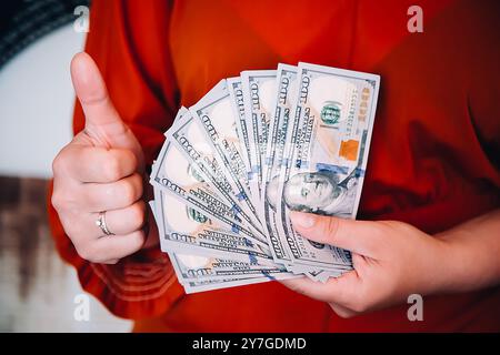 A person, with great enthusiasm, is proudly showing off cash while giving a thumbs up gesture of approval Stock Photo