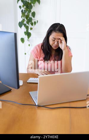 Working from home, woman feeling stressed while using laptop and desktop computer Stock Photo