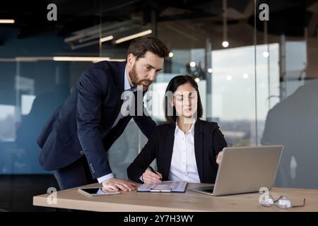 Two business professionals working together in office, analyzing data on laptop. Man and woman collaborating on project, showcasing teamwork, focus, and productivity. Stock Photo