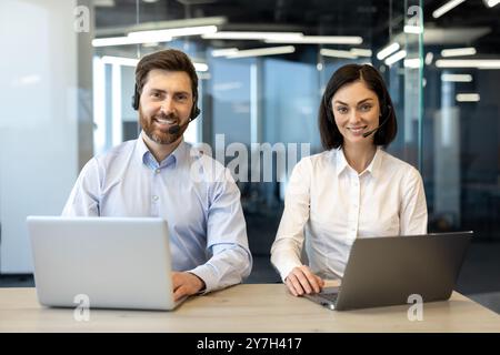 Friendly customer support representatives using laptops engaged in communication with clients. Office professionals showcasing teamwork and efficiency in a modern workspace. Stock Photo