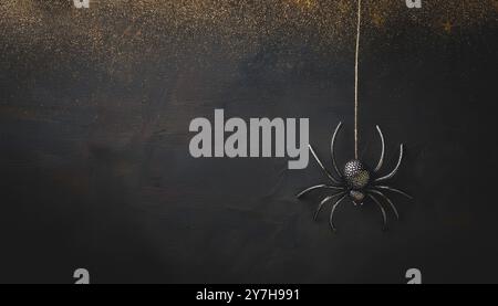 Hanging black glitter spider decoration for halloween, dark grunge gold glitter background, spooky, minimalist night scene, creepy insect suspended in Stock Photo