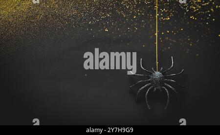 Hanging black glitter spider decoration for halloween, dark grunge gold glitter background, spooky, minimalist night scene, creepy insect suspended in Stock Photo